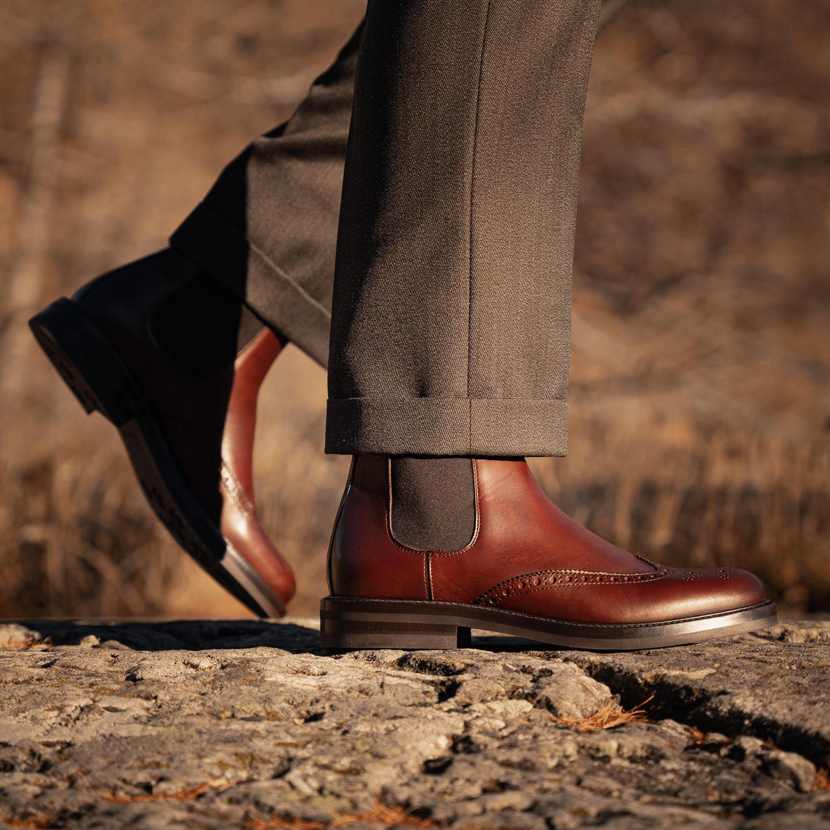 Brown Leather Brogue Chelsea Boots worn outdoors, showcasing stylish craftsmanship on rocky terrain.