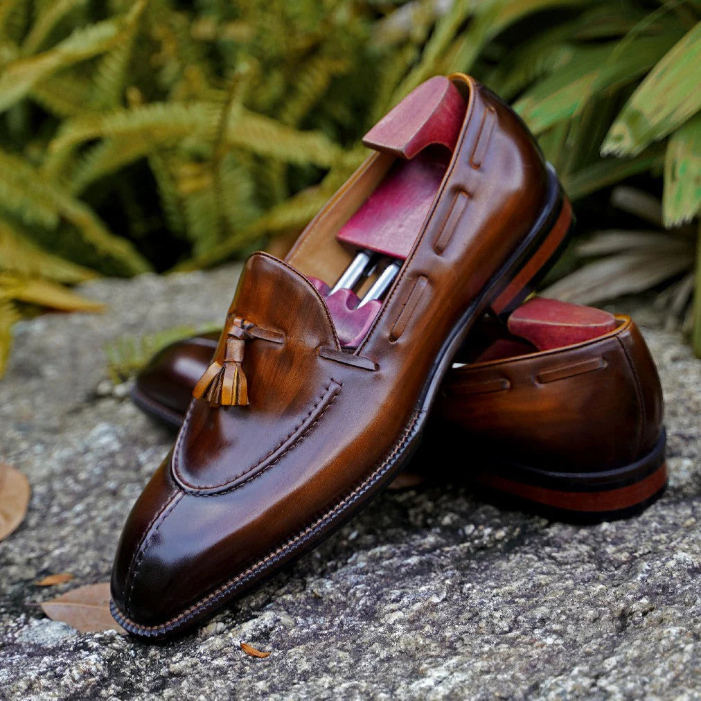 Close-up of Brown Patina Leather Tassel Loafers, showcasing the polished leather, detailed stitching, and stylish tassel accent against a natural outdoor background.