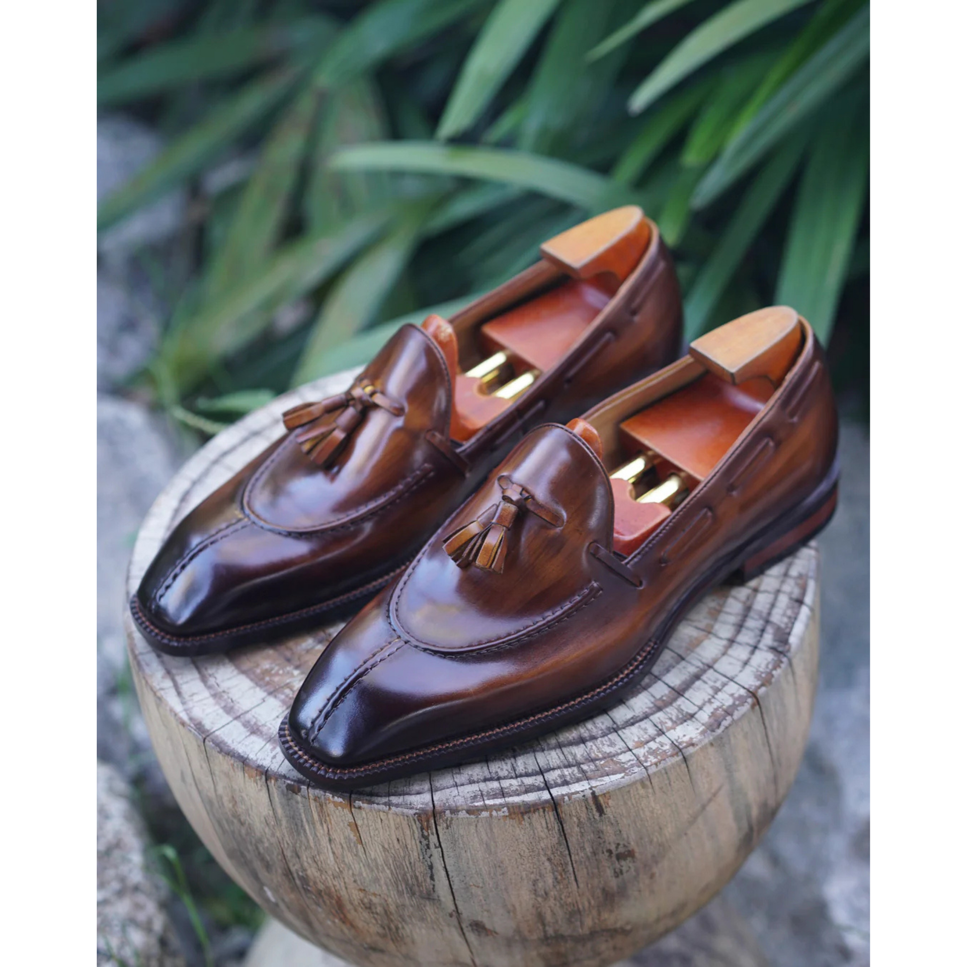 Brown Patina Leather Tassel Loafers displayed on a wooden surface, showcasing the elegant tassel detail, polished leather finish, and wooden shoe trees inside.