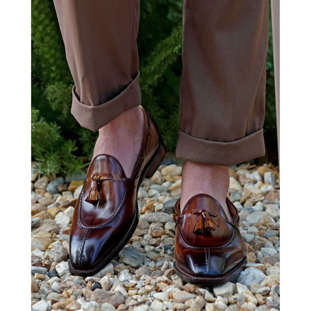 Brown Patina Leather Tassel Loafers worn with rolled-up brown trousers, showcasing the polished leather finish and stylish tassel detailing in a natural outdoor setting.