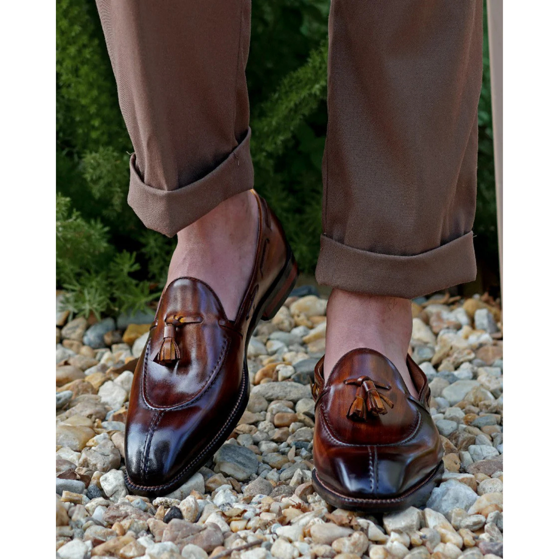 Brown Patina Leather Tassel Loafers worn with rolled-up brown trousers, showcasing the polished leather finish and stylish tassel detailing in a natural outdoor setting.