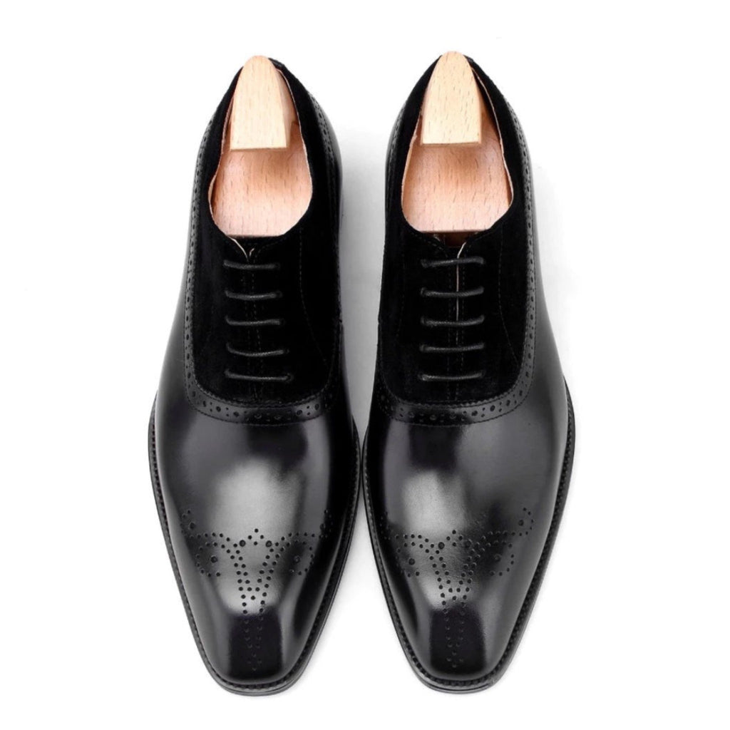 Top view of men’s black suede and leather oxford shoes, showcasing intricate brogue detailing and a smooth, polished finish.