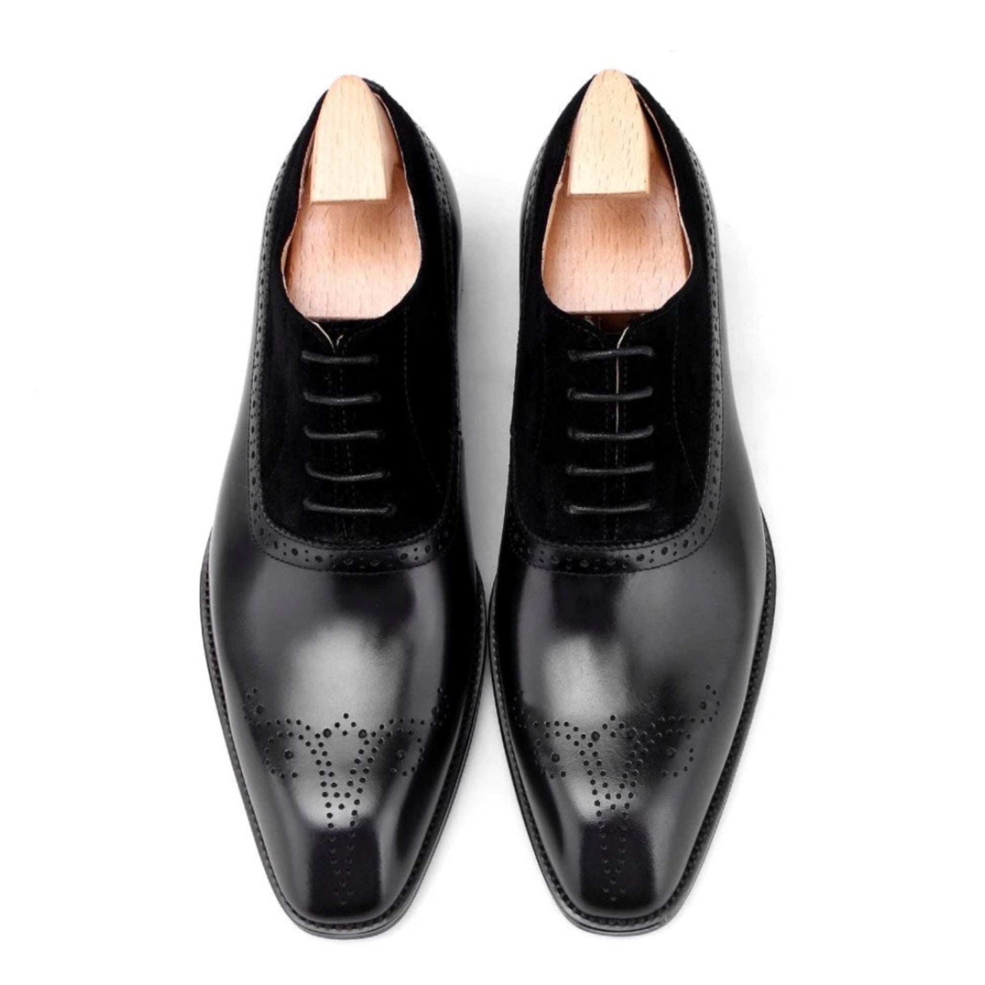 Top view of men’s black suede and leather oxford shoes, showcasing intricate brogue detailing and a smooth, polished finish.