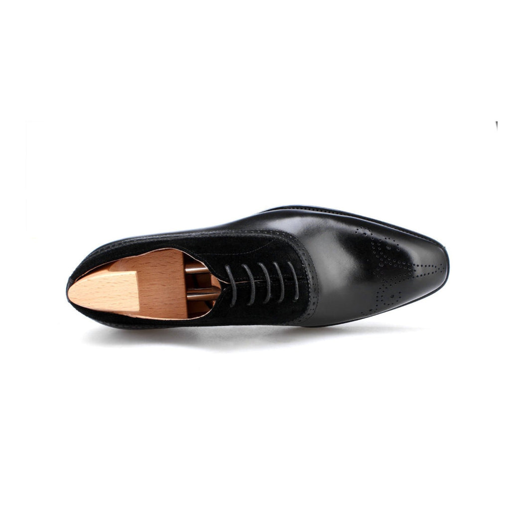 Top-down view of black suede and leather oxford shoes with elegant brogue perforations and wooden shoe trees.