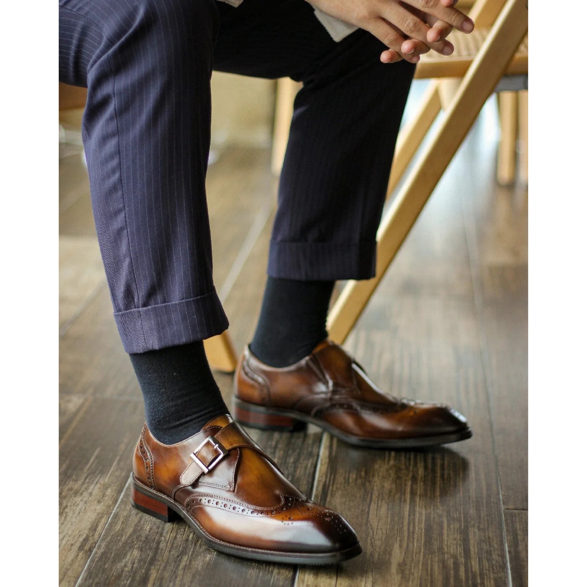 Side view of tan leather single monk strap shoes with brogue detailing, worn with formal attire.